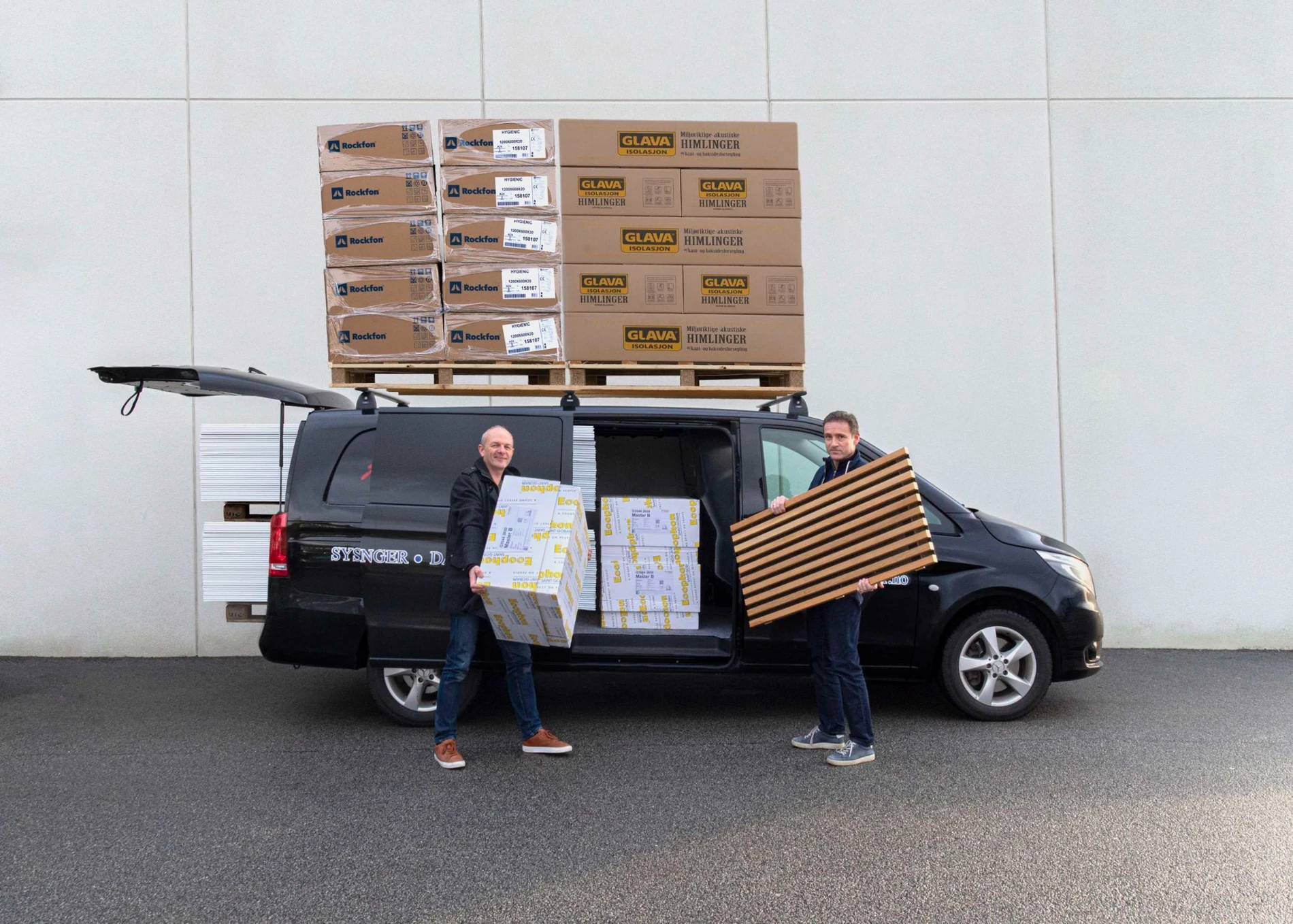 To ansatte ved firmabilen med himlingsplater og trespiler.