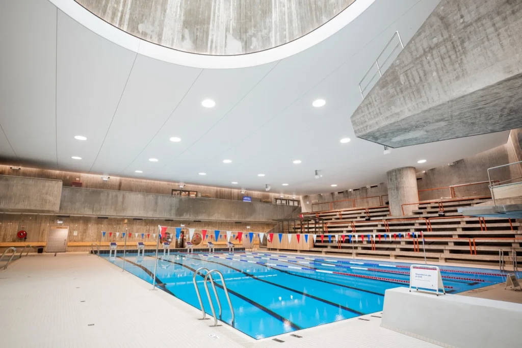 Lys akustisk himling over basseng og tribuner i en svømmehall.